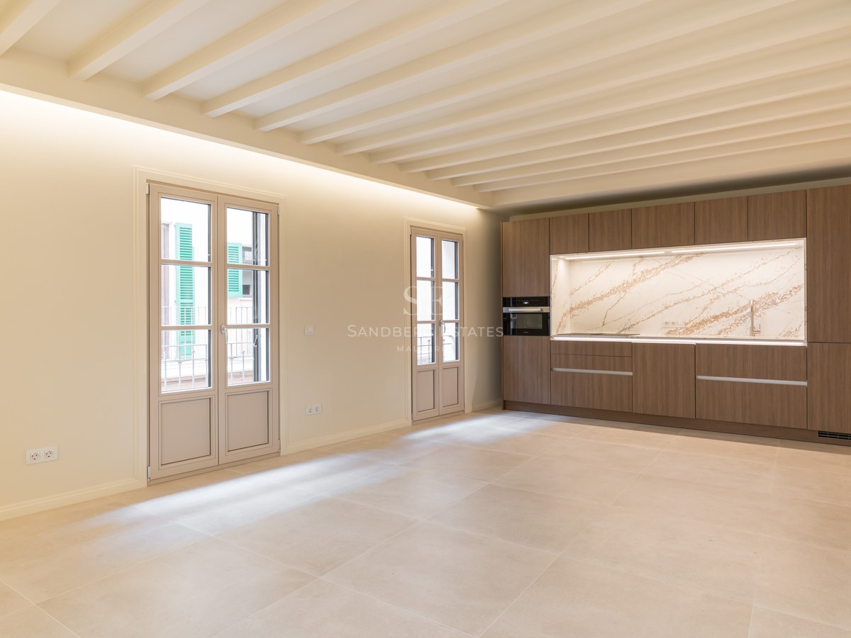 Cocina moderna con muebles de madera, encimera de mármol veteado, techos de vigas blancas y suelo de gres porcelánico.