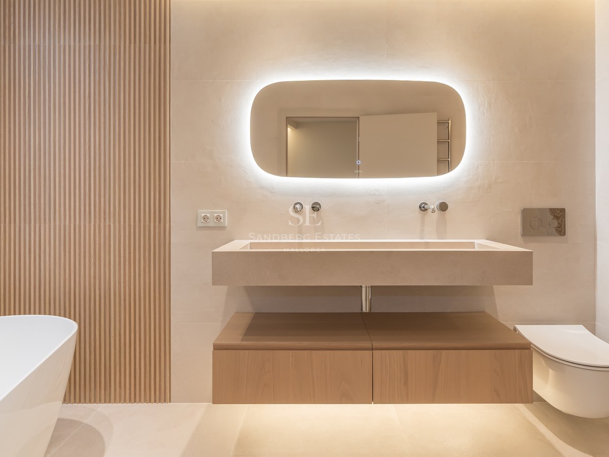 Baño contemporáneo con lavabo flotante de piedra, espejo retroiluminado, paneles de madera y bañera exenta.