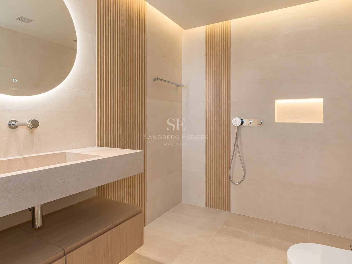 Baño moderno con espejo circular retroiluminado, lavabo de piedra integrada y paneles de madera verticales.