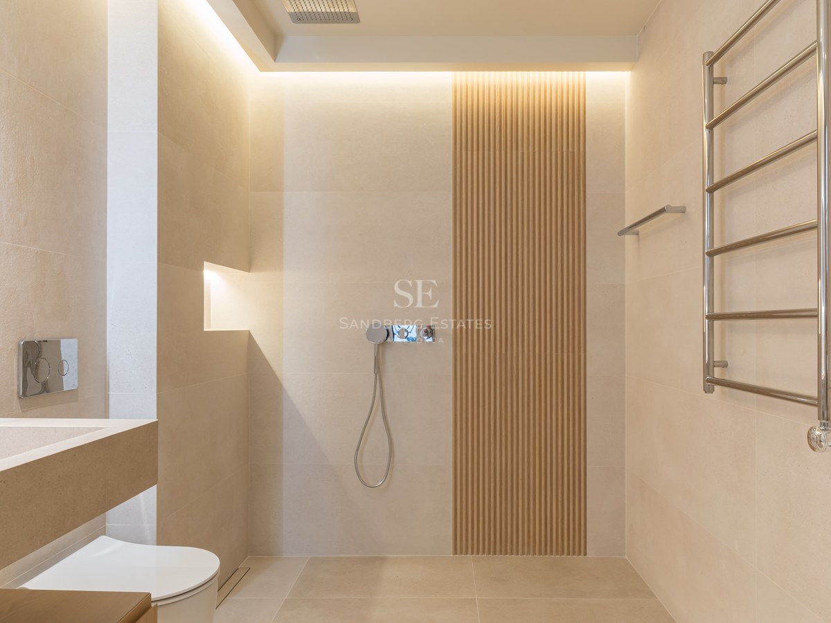 Baño moderno con azulejos beige, pared de listones de madera, ducha italiana y toallero de cromo.
