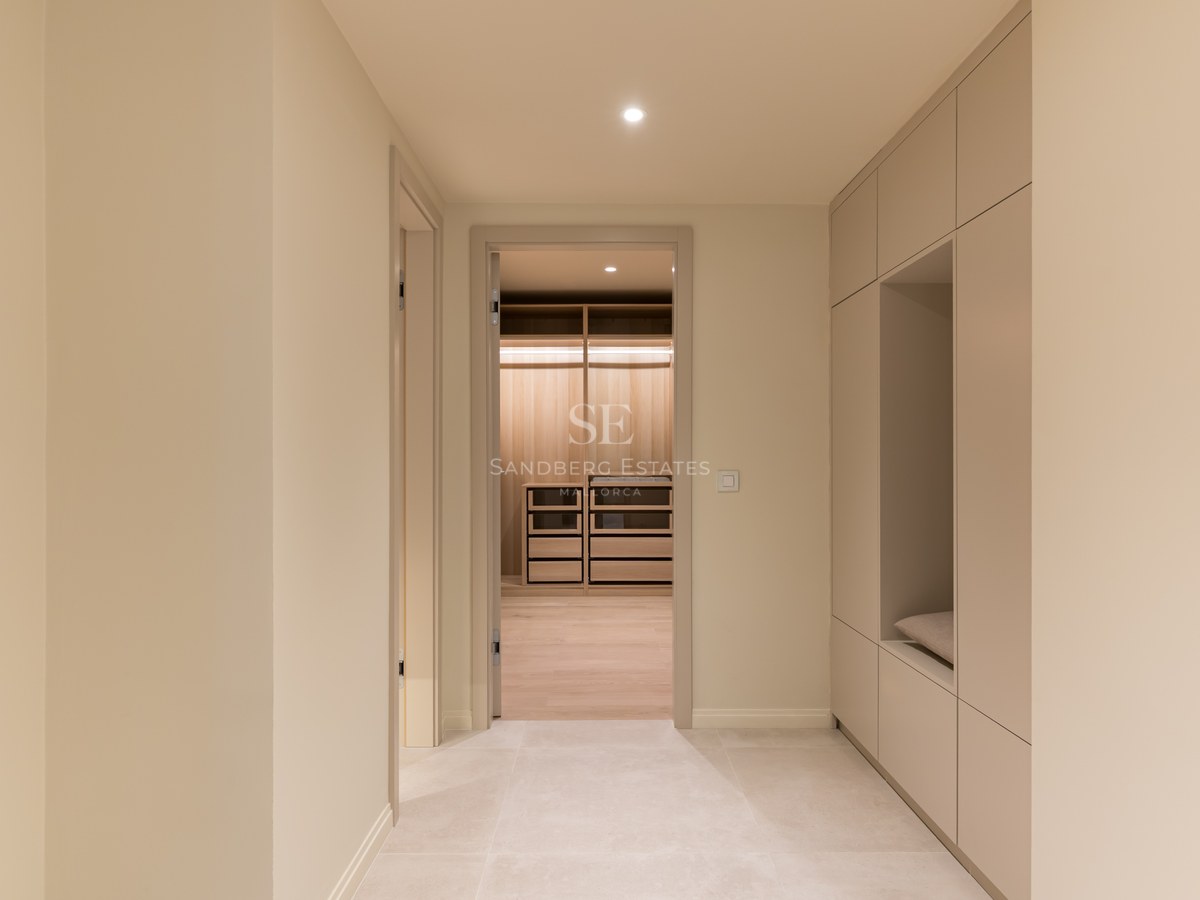 Pasillo con armarios minimalistas beige y banco integrado que conduce a un vestidor de madera iluminado.