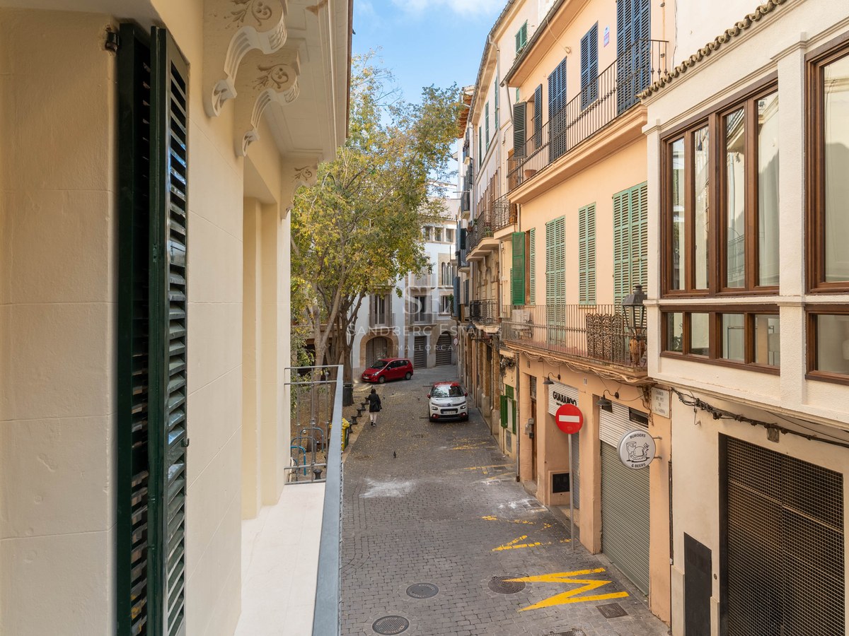 Calle estrecha empedrada con fachadas históricas y persianas mallorquinas tradicionales bajo un cielo despejado.