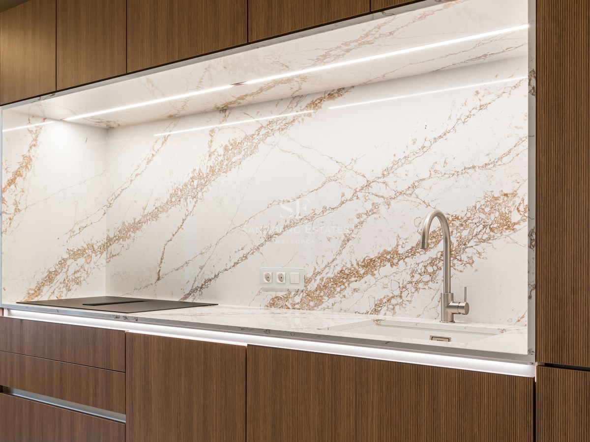 Cocina moderna con armarios de madera oscura, salpicadero de mármol con vetas marrones e iluminación LED integrada.