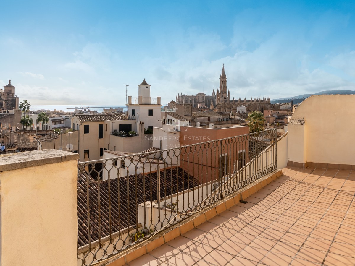 Terraza soleada con suelos de terracota y barandilla de forja con vistas a Palma de Mallorca y su catedral.