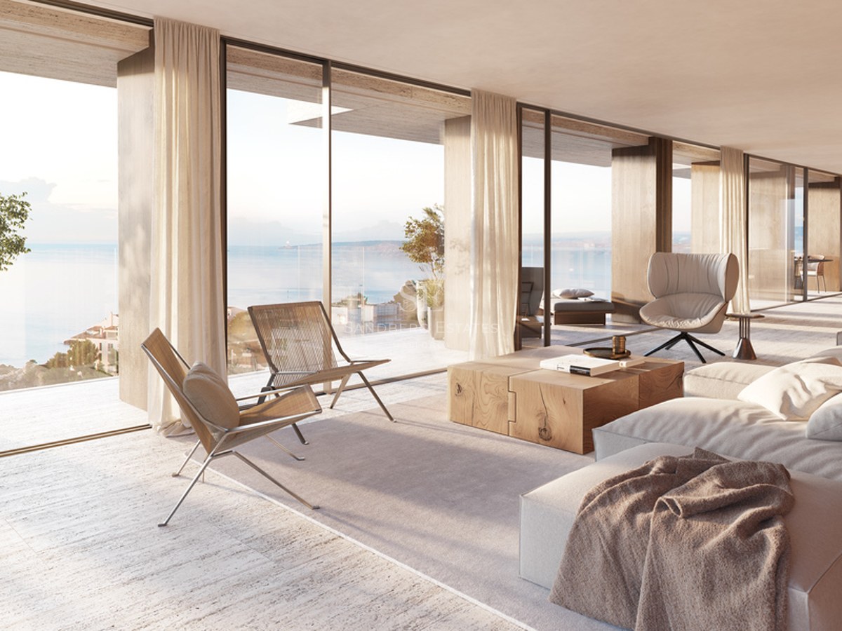 Bright living room with floor-to-ceiling glass doors overlooking the sea, featuring travertine floors and modern furniture.