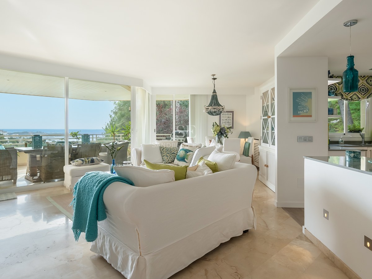 Contemporary living room with marble floors, white sofas, and turquoise accents leading to a sea-view terrace.