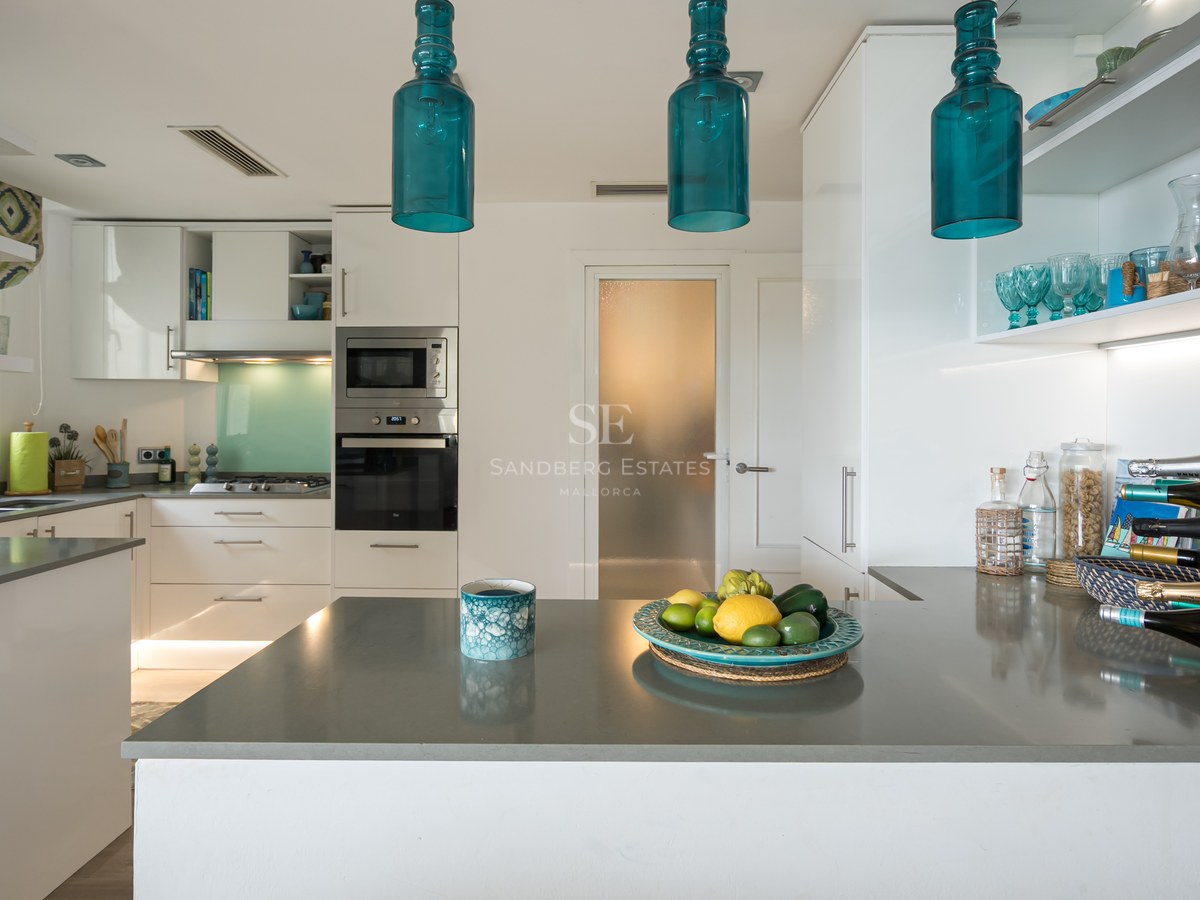 Modern white kitchen with grey countertops, turquoise glass pendant lights, and integrated appliances.
