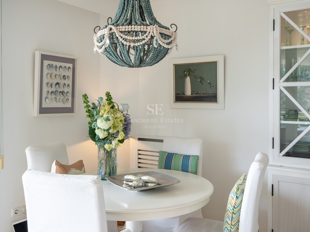 White round table, slipcovered chairs, blue beaded chandelier, and built-in cabinet in a bright dining area.