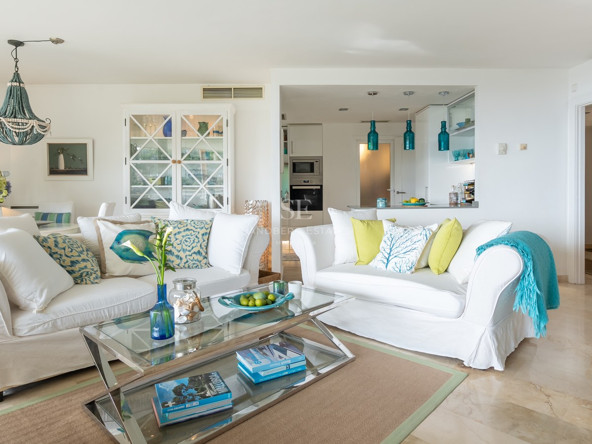 Bright living room with two white sofas, a glass coffee table, marble floors, and Mediterranean decor elements.