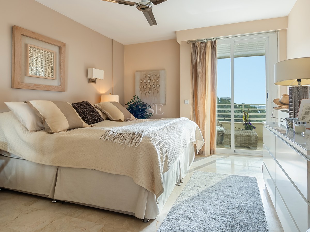 Bright bedroom with cream bedding, marble floors, and sliding glass doors opening to a sunlit terrace.