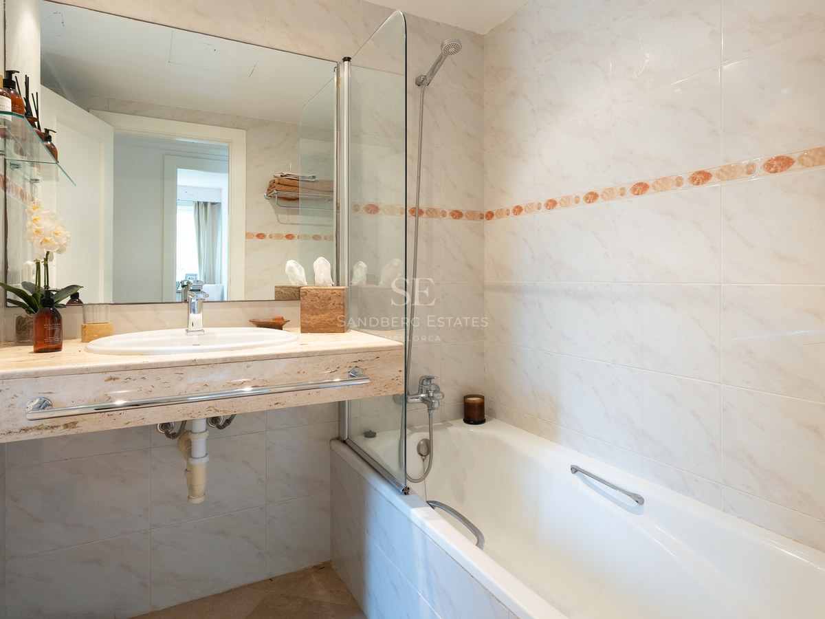 Bathroom featuring a bathtub with glass screen and a cream-colored marble vanity with an inset sink.