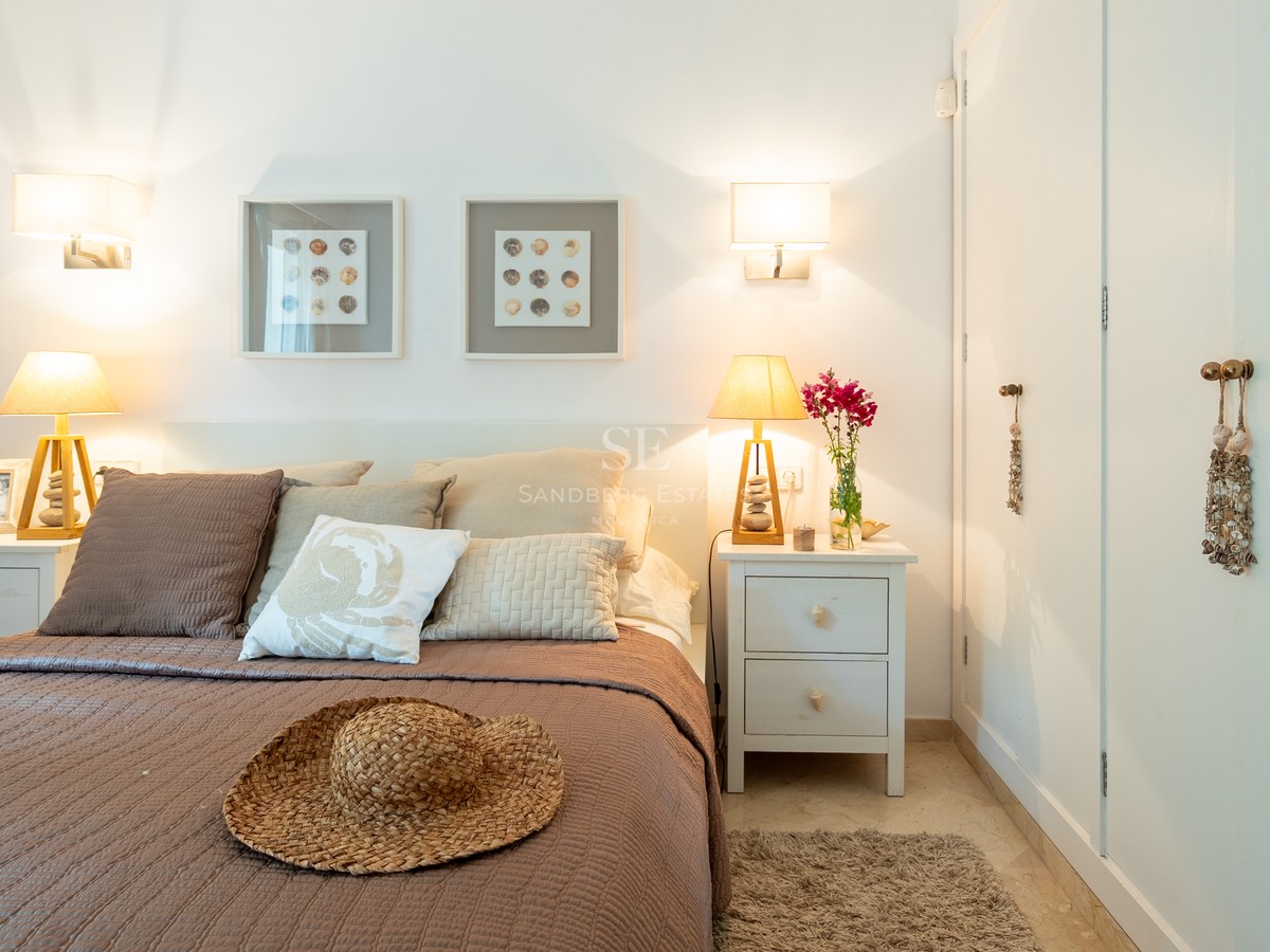 Bright bedroom featuring a large bed, wooden lamps, built-in white wardrobes, and coastal-themed decor.