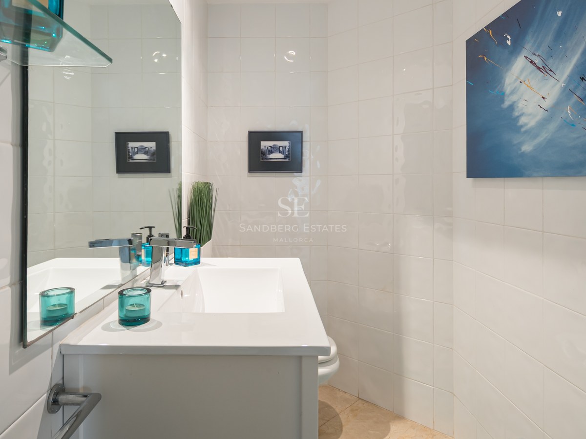 White tiled bathroom with a white vanity sink, chrome faucet, large mirror, and blue abstract wall art.