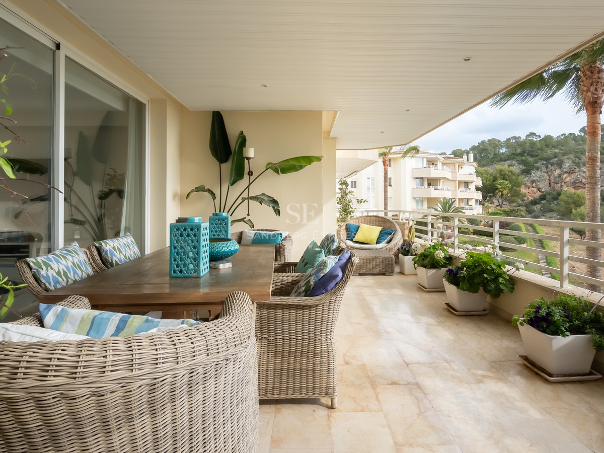 Spacious covered terrace with marble floors, wicker dining furniture, and views of lush hills and palm trees.