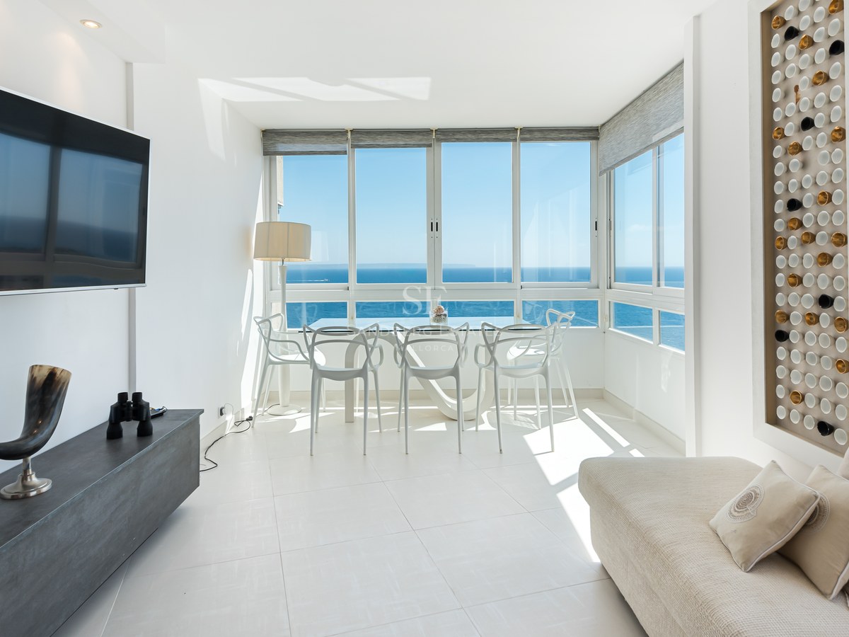 Bright modern living room featuring full-length windows with panoramic views of the Mediterranean sea and white furniture.