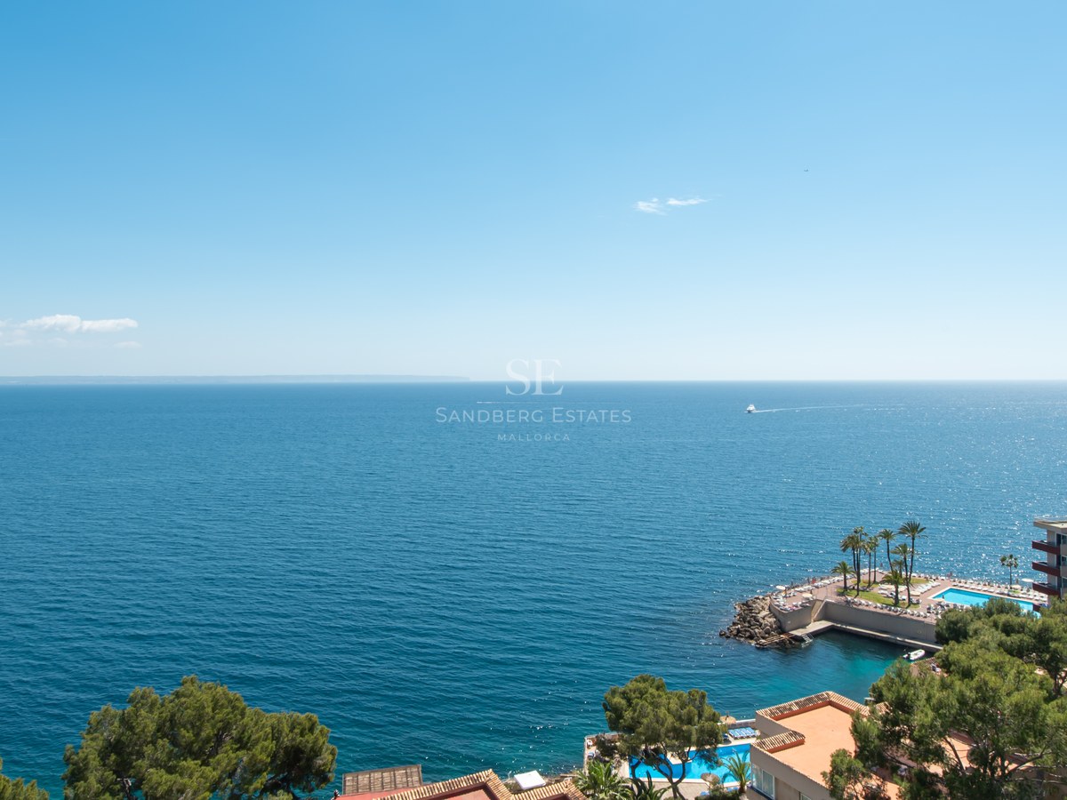 High-angle view of the blue Mediterranean sea with coastline buildings and swimming pools under a clear sky.