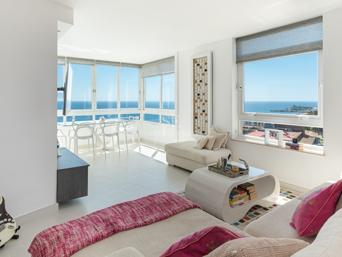 Bright modern living room featuring white furniture, pink accents, and large windows overlooking the Mediterranean sea.