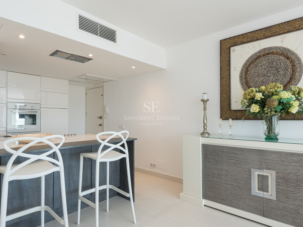 Modern white kitchen featuring a charcoal grey island, white designer bar stools, and a stylish sideboard.