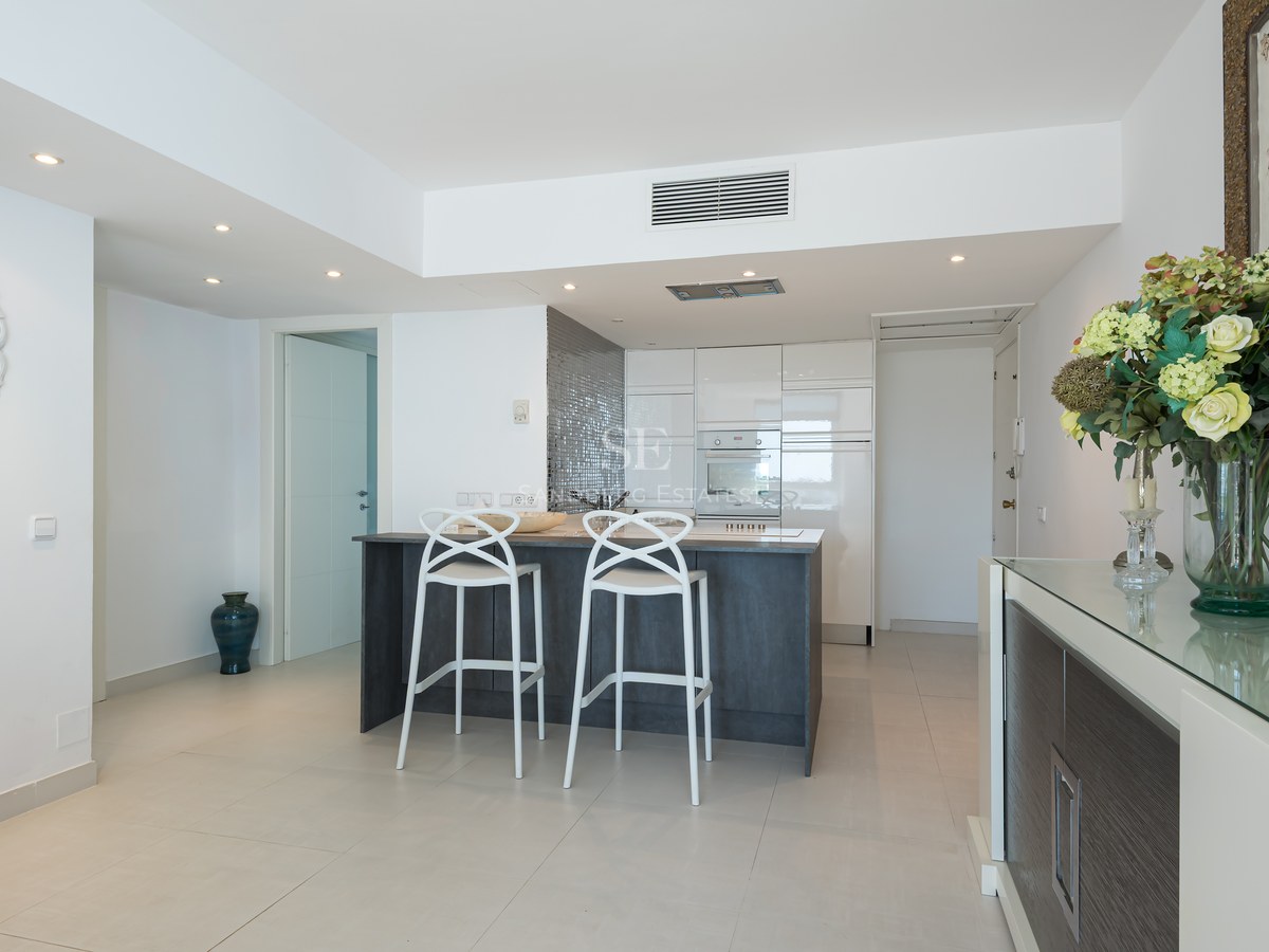 Modern open-plan kitchen featuring a dark grey island, white designer stools, and high-gloss cabinetry.
