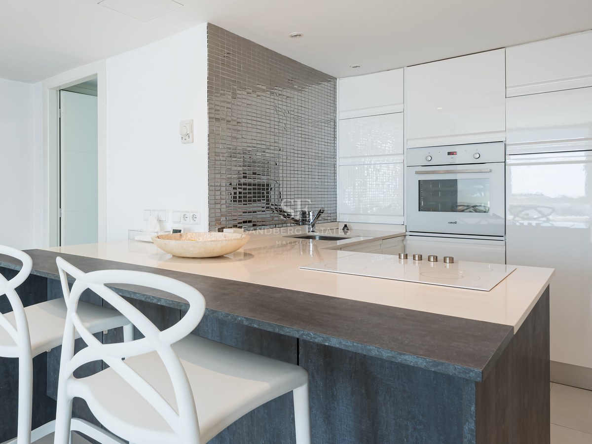 Contemporary white kitchen featuring a dark breakfast bar, white designer chairs, and a silver mosaic backsplash.