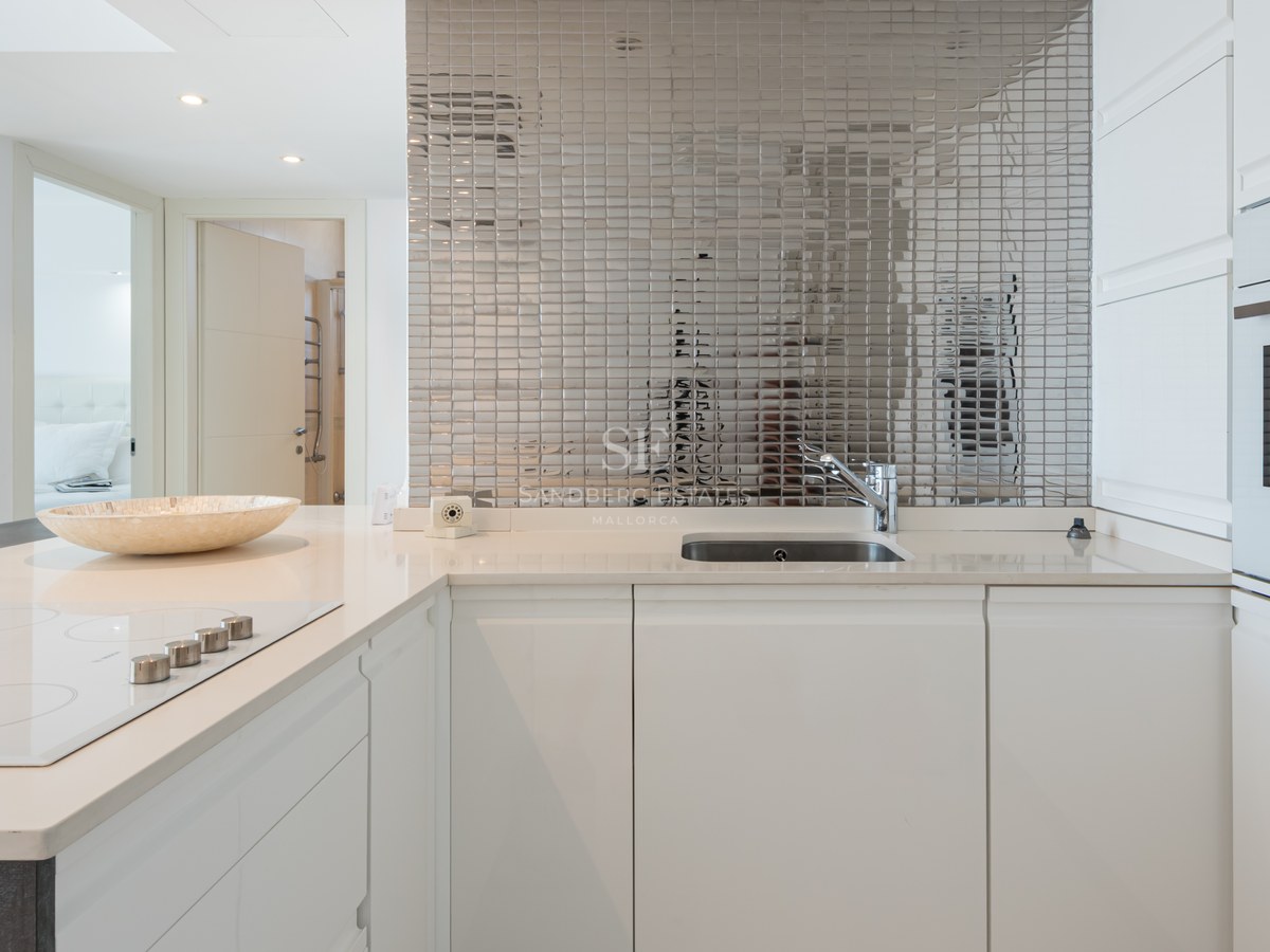Bright white modern kitchen featuring a mirrored mosaic backsplash, quartz countertops, and integrated appliances.