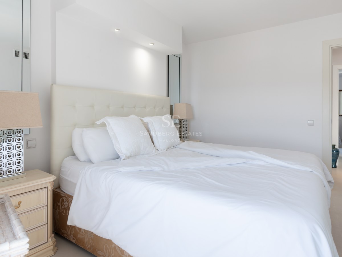 Bright bedroom featuring a white tufted headboard, symmetric bedside tables with lamps, and clean tiled floors.