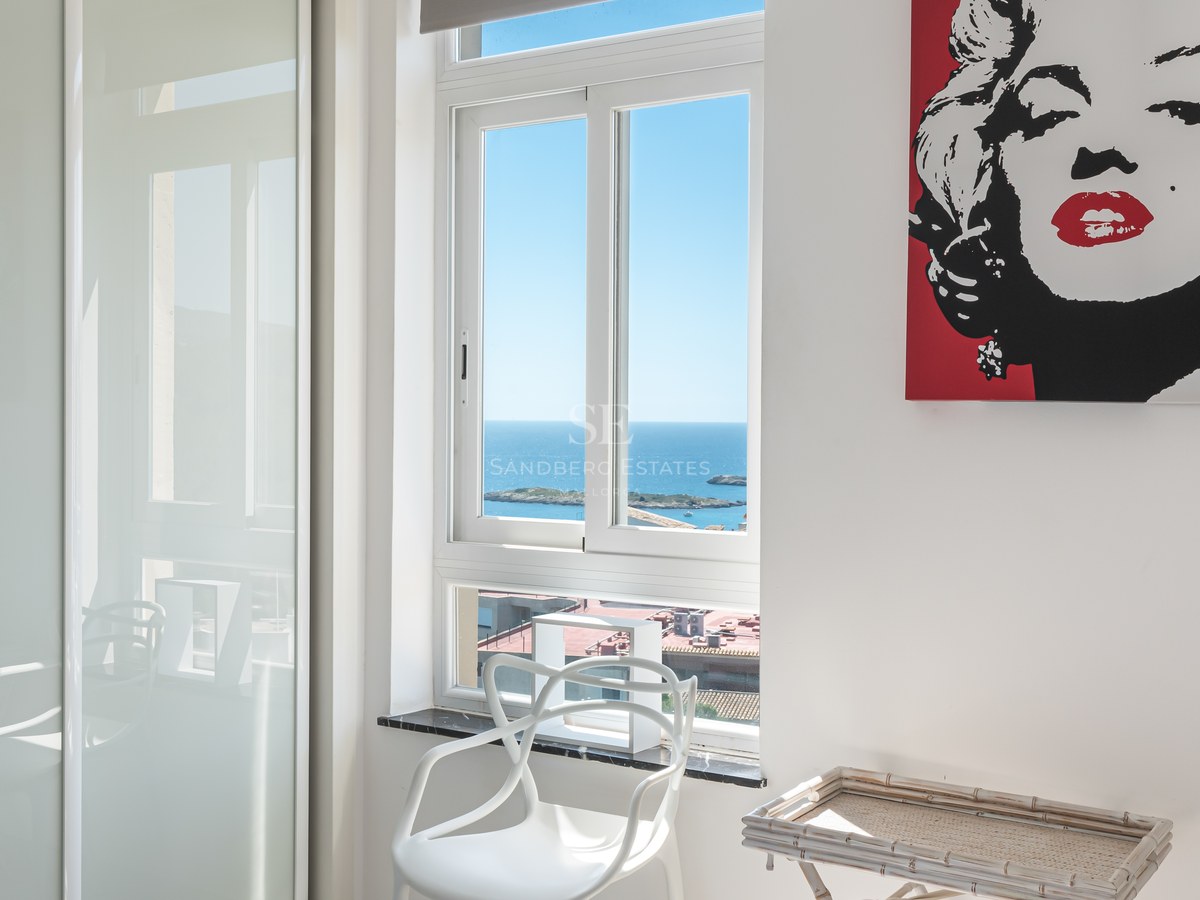 Bright white bedroom with a window overlooking the Mediterranean sea and sleek fitted wardrobes.
