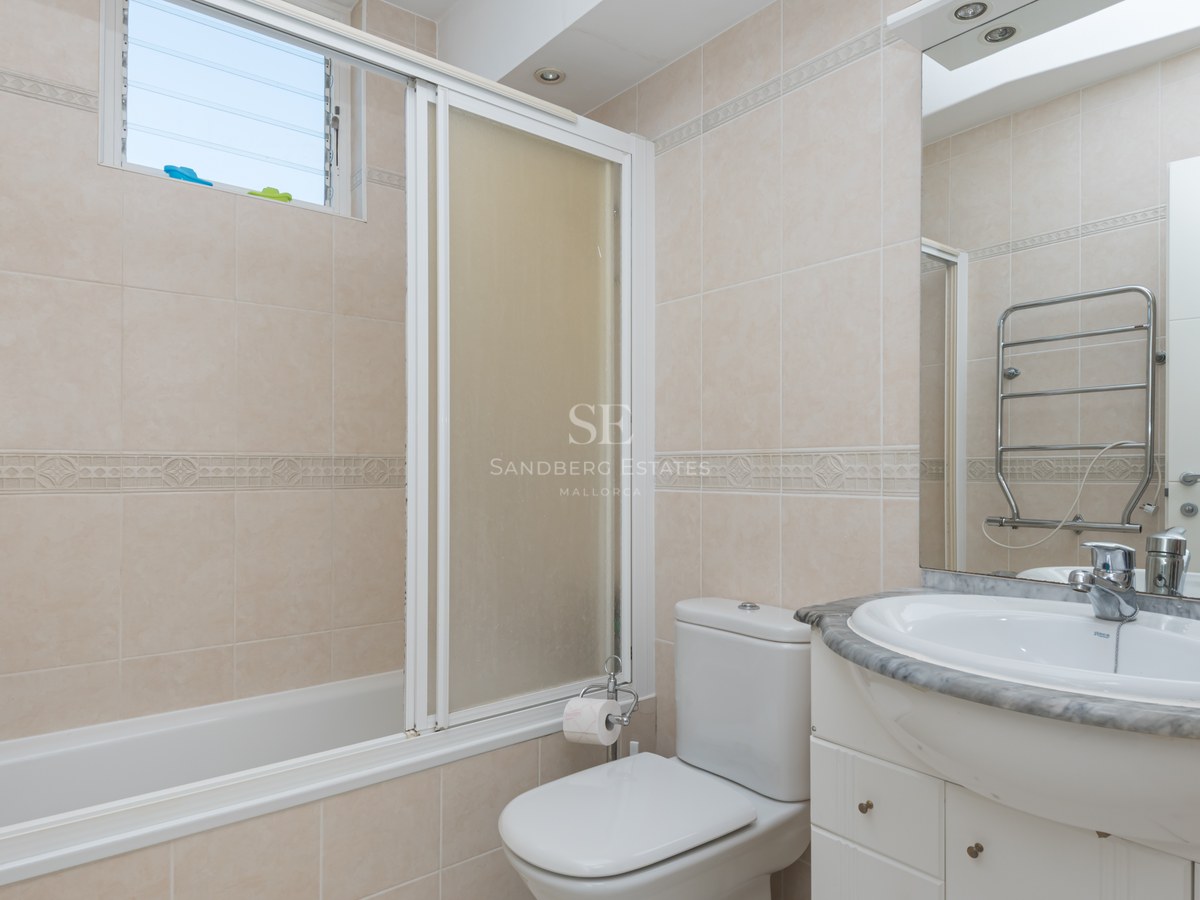 Bright bathroom featuring a bathtub with a screen, a marble vanity unit, a white sink, and neutral ceramic wall tiles.