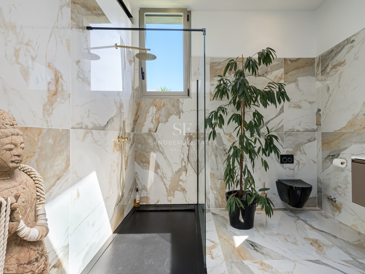 Modernes Badezimmer mit Marmorfliesen, schwarzer begehbarer Dusche, goldenen Armaturen und einer Buddha-Steinfigur.