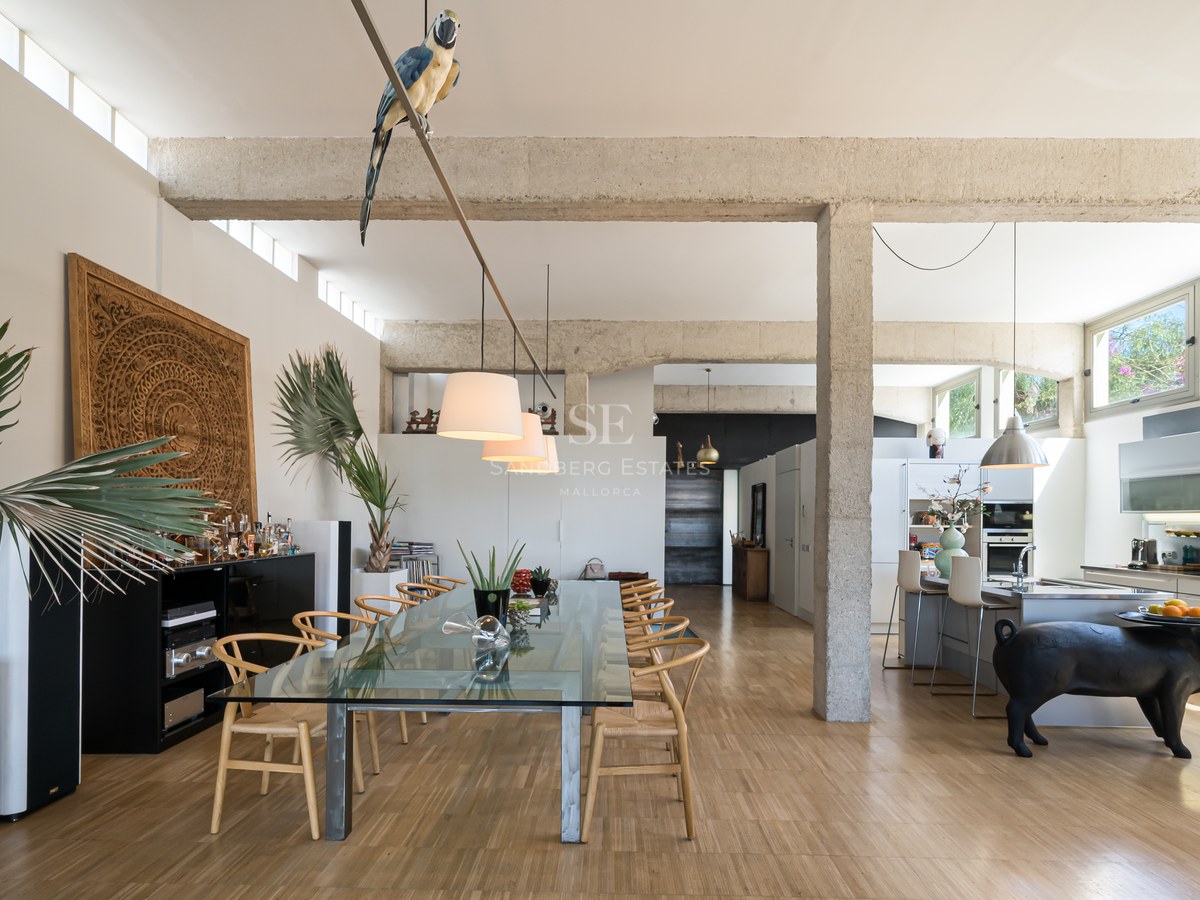 Offener Essbereich mit Sichtbetonbalken, großem Glastisch und moderner Küche in lichtdurchflutetem Loft.