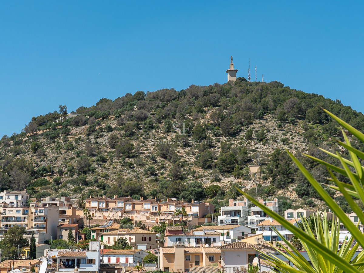 Blick auf einen grünen Hügel mit einem Monument an der Spitze, über einer mediterranen Stadt unter klarem blauem Himmel.