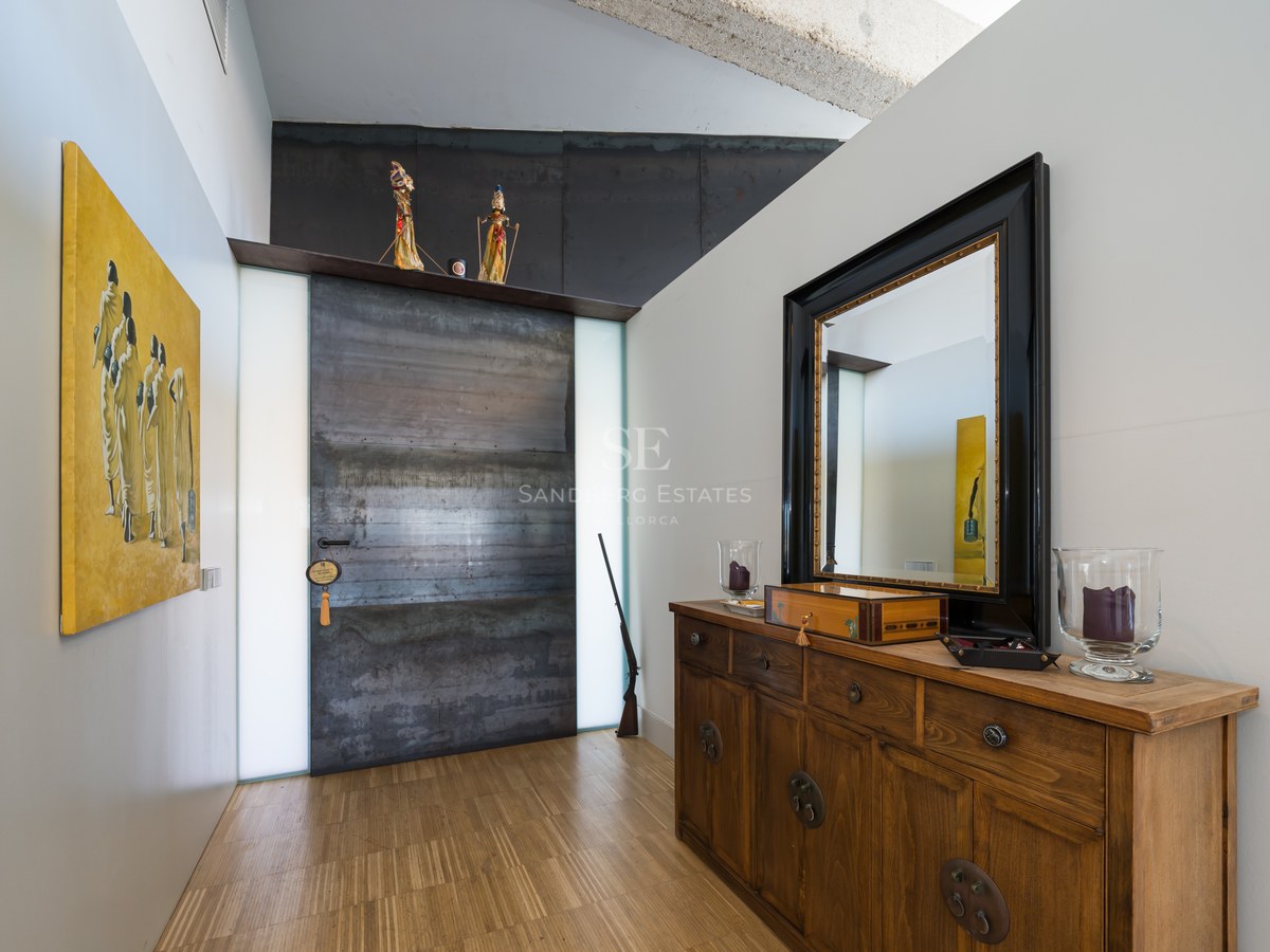 Flur mit großer industrieller Stahltür, Sideboard aus Holz mit Spiegel und zeitgenössischer Kunst.