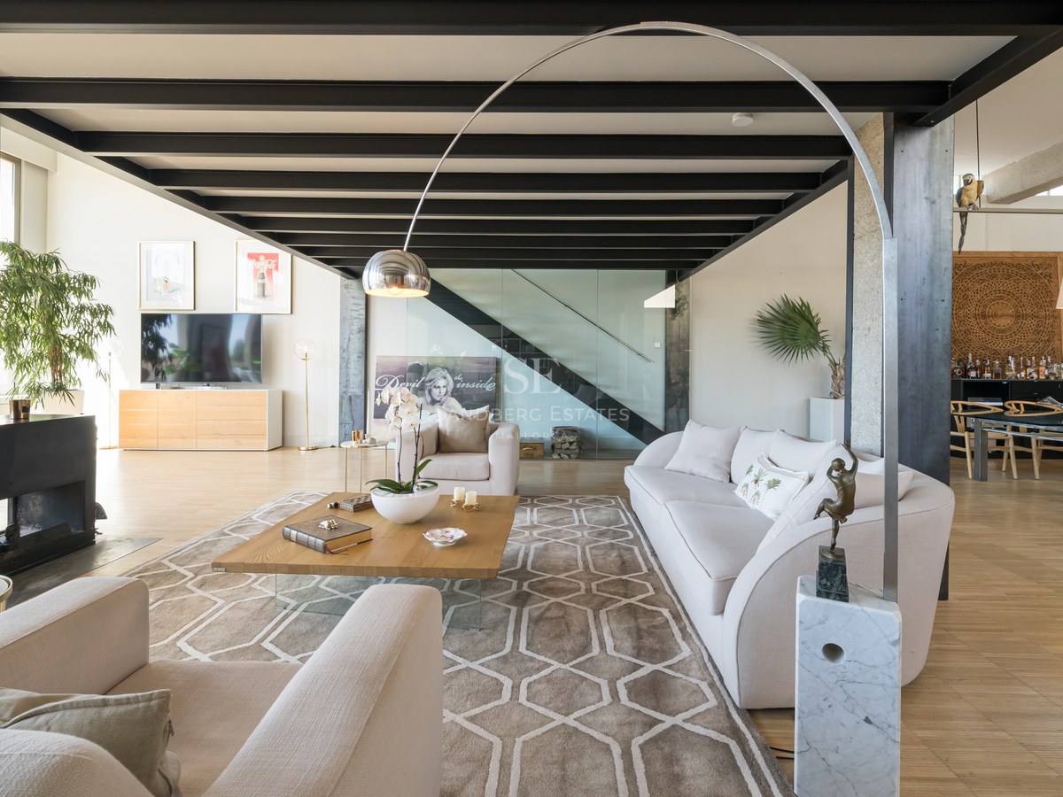 Großzügiges modernes Wohnzimmer mit schwarzen Stahlbalken, cremefarbenem Sofa und gläsernem Treppenhaus.
