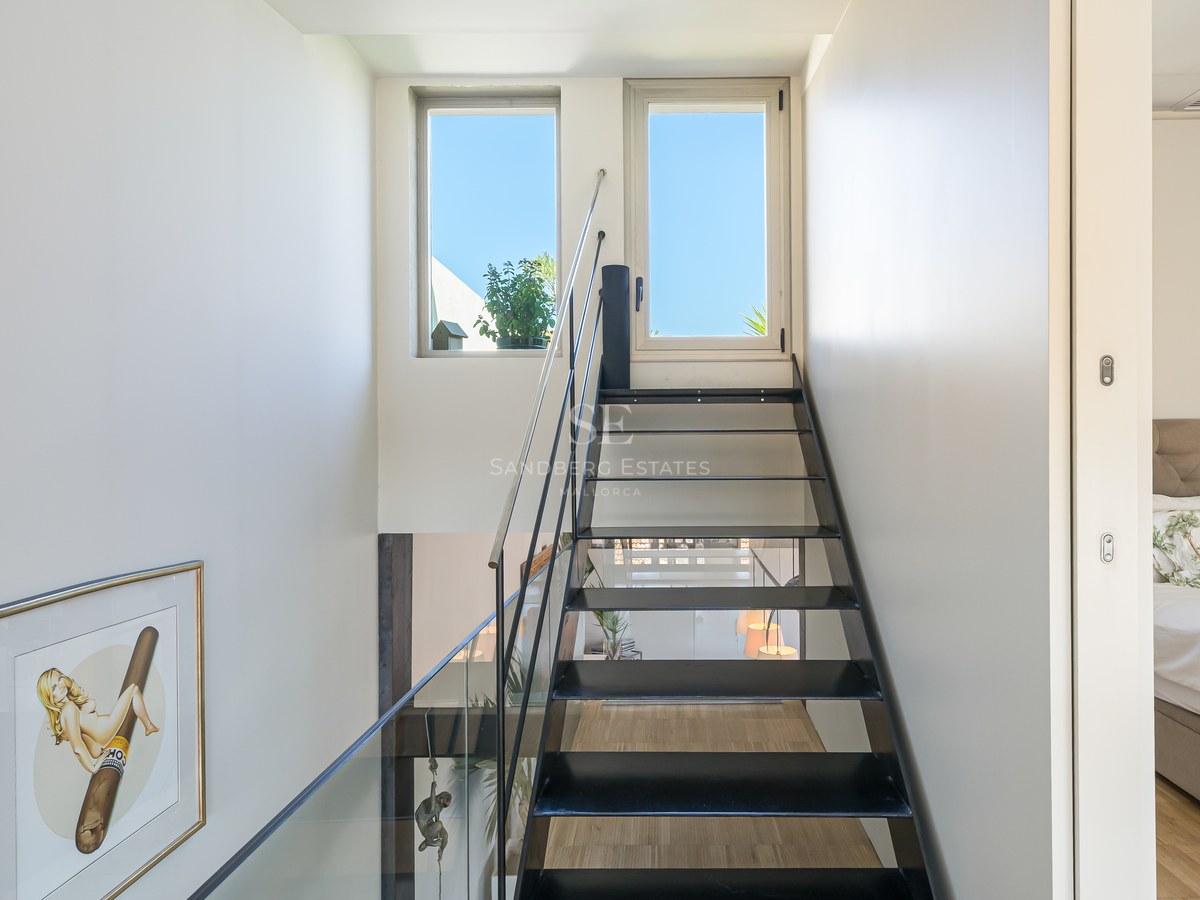 Schwarze Stahltreppe mit Glasgeländer und Blick auf den blauen Himmel durch die oberen Fenster.