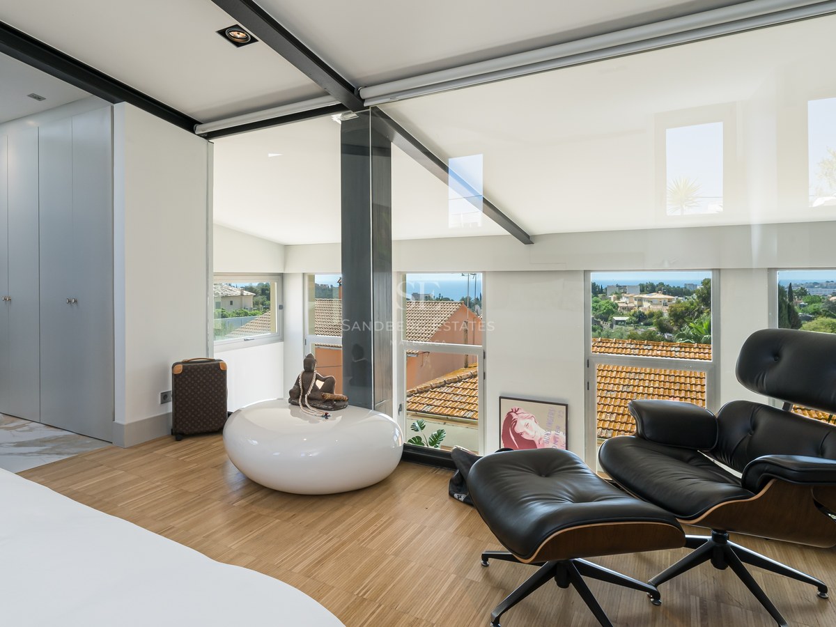 Modernes Schlafzimmer mit Eames Lounge Chair, Eichenparkett und Glasfronten mit Blick auf das Meer und die Stadt.