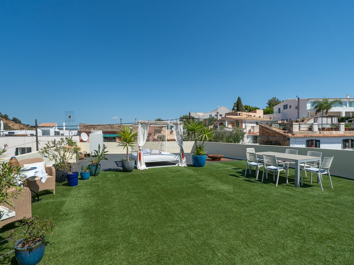 Dachterrasse mit Kunstrasen, weißem Balinesischem Bett, Essbereich im Freien und Blick auf weiße Dorfhäuser.