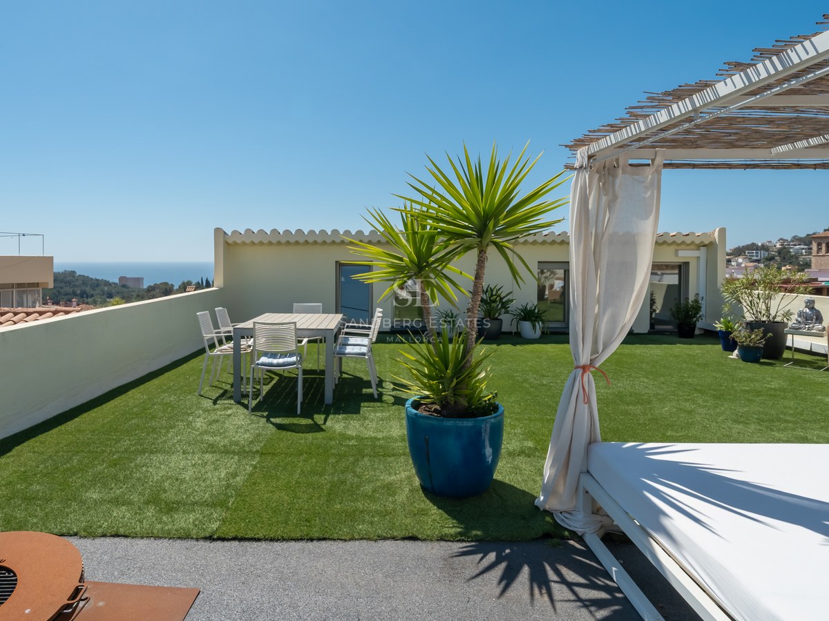 Dachterrasse mit Kunstrasen, einem Daybed unter einer Bambus-Pergola und einem Esstisch mit Blick auf das Meer.