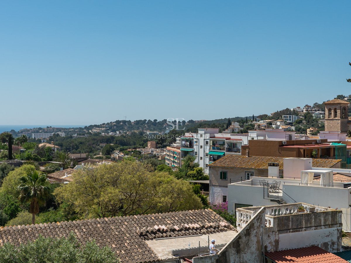 Blick über mediterrane Dächer, grüne Hügel und das ferne blaue Meer unter klarem Himmel.