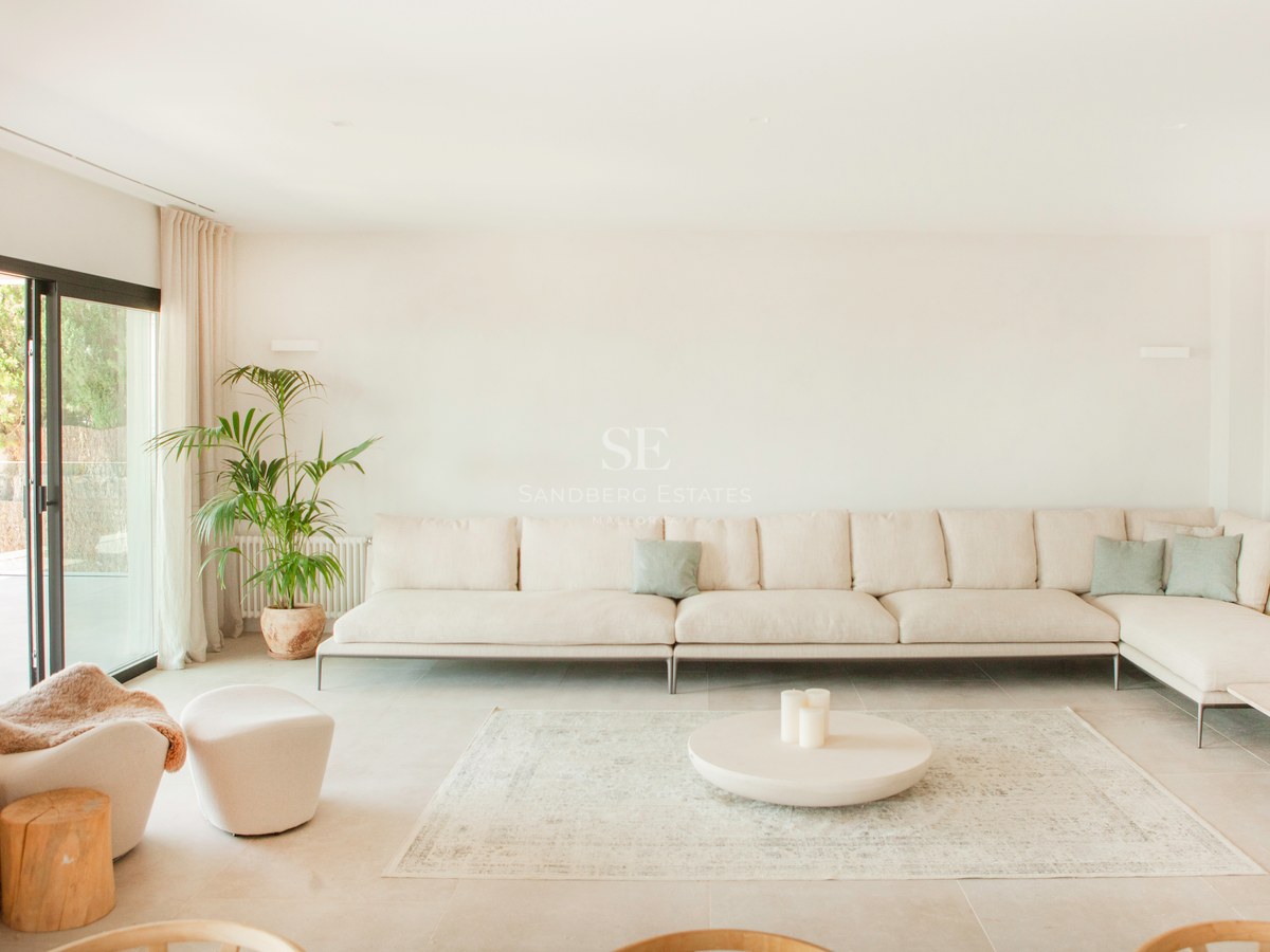 Helles Wohnzimmer mit großem beigem Ecksofa, rundem Couchtisch auf Teppich und Glasschiebetüren zur Terrasse.