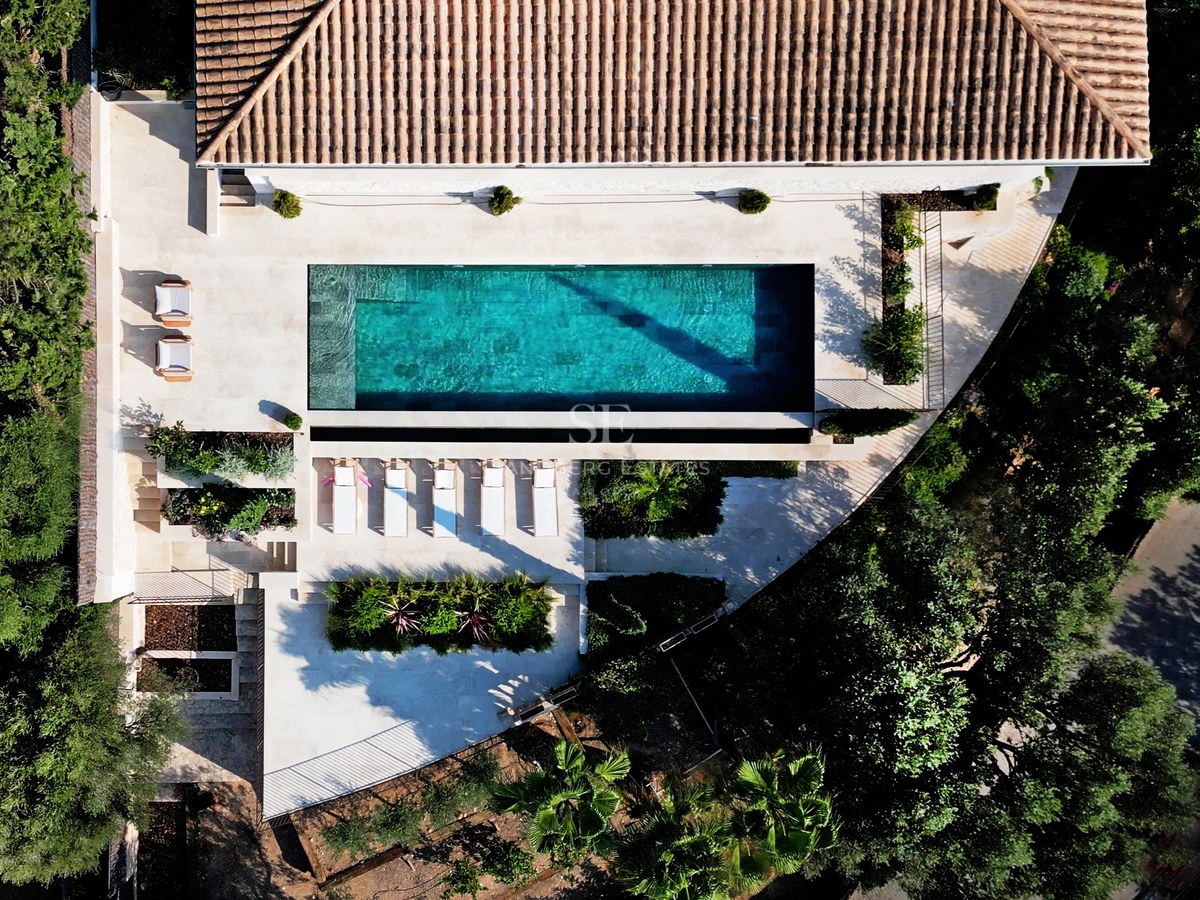 Draufsicht auf einen türkisfarbenen Pool, umgeben von Steinterrassen, Sonnenliegen und üppiger mediterraner Vegetation.