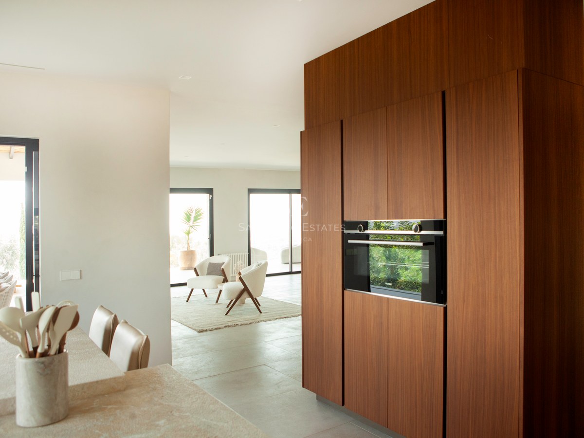 Moderne Küche mit Walnussholzschränken, Einbaubackofen und Steininsel mit Blick auf das helle Wohnzimmer.