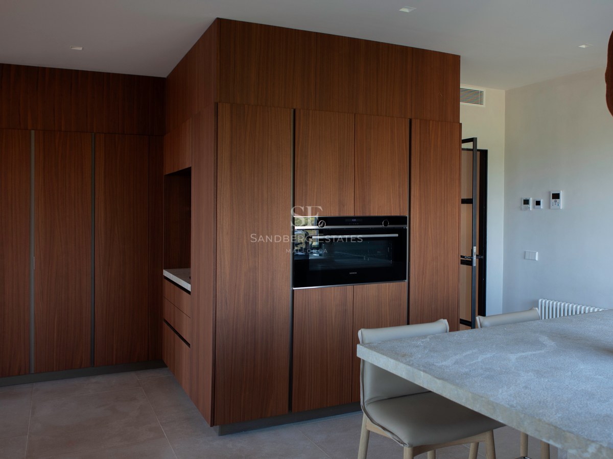 Moderne Küche mit raumhohen Walnussholz-Schränken, integriertem Backofen und Steininsel mit Lederstühlen.