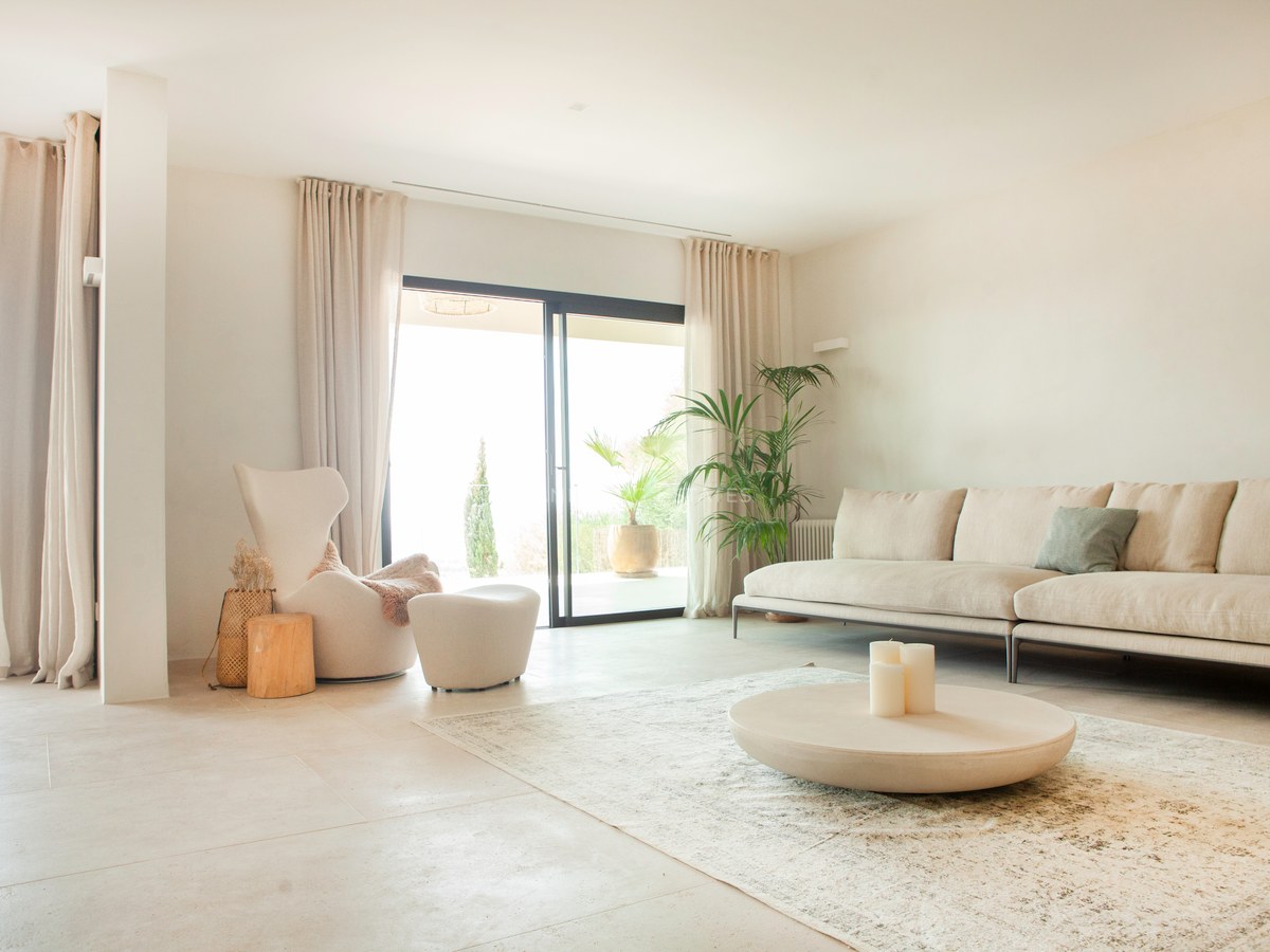 Helles Wohnzimmer mit beige Sofa, Steincouchtisch und bodentiefe Fensterfronten zur Terrasse.