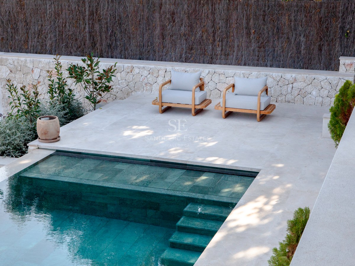 Draufsicht auf einen modernen Pool mit türkisfarbenen Fliesen neben einer Steinterrasse mit zwei Holzsesseln.