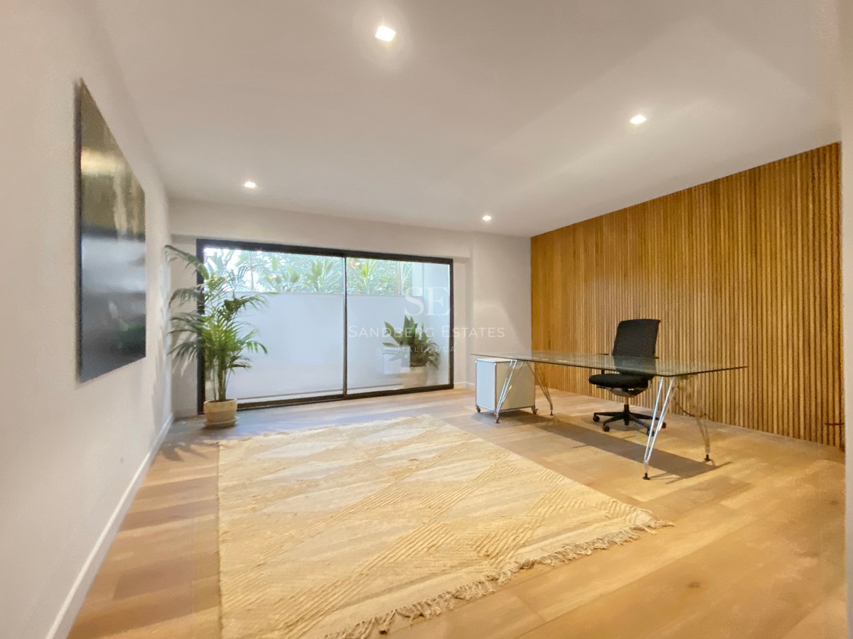 Modernes Arbeitszimmer mit Glastisch, Holzlamellenwand und Glasschiebetür zu einem kleinen Innenhof.