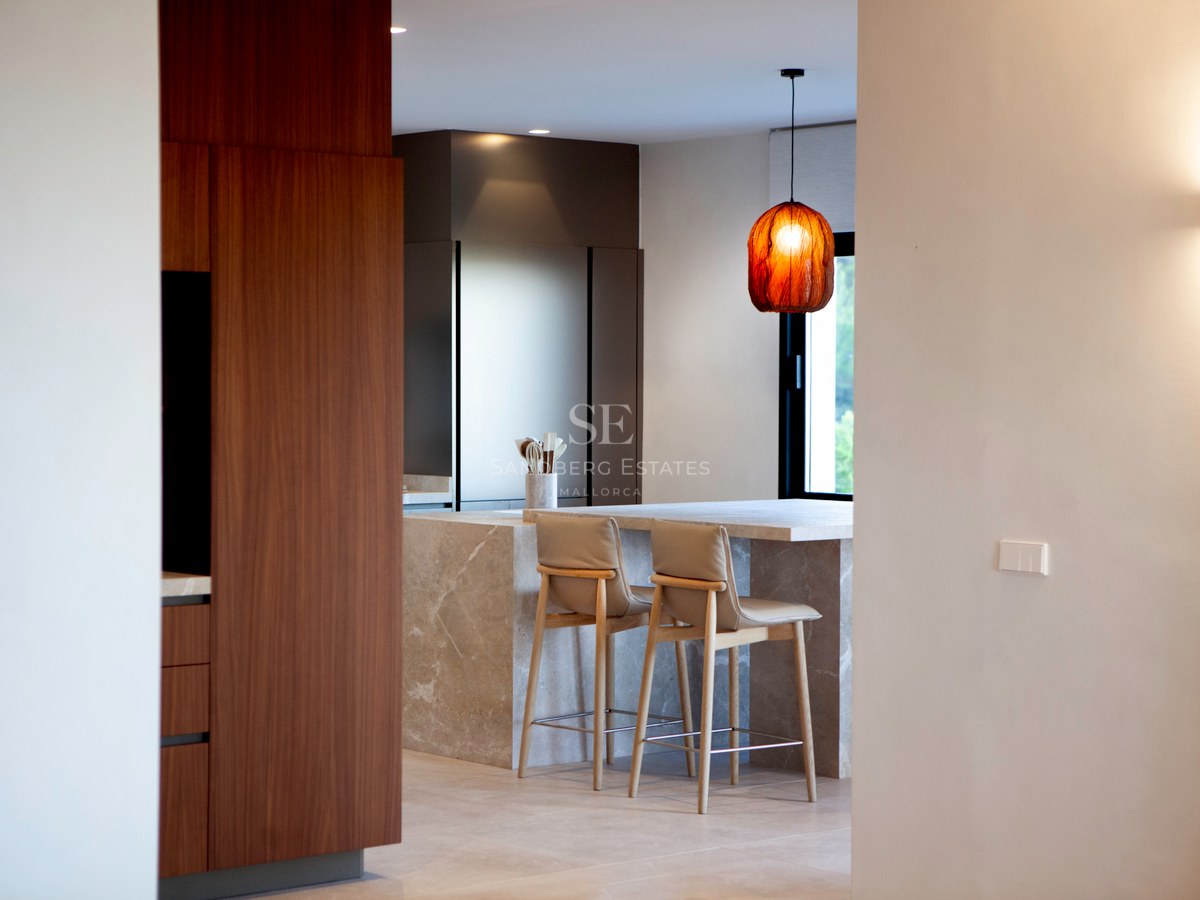 Moderne Küche mit großer Steininsel, Barhockern, Schränken aus Walnussholz und Designer-Leuchte.