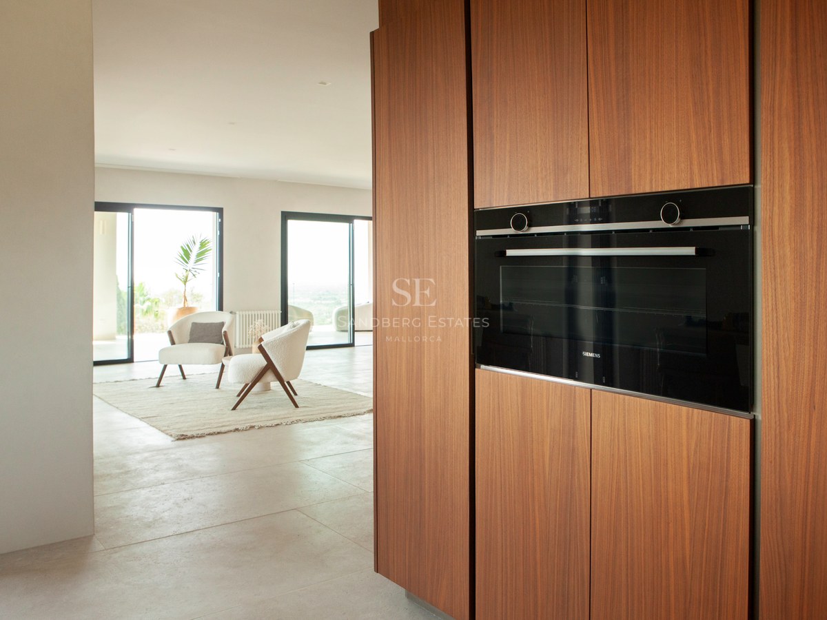 Nahaufnahme von Walnussholz-Küchenschränken mit eingebautem Siemens-Backofen mit Blick auf ein helles Wohnzimmer.
