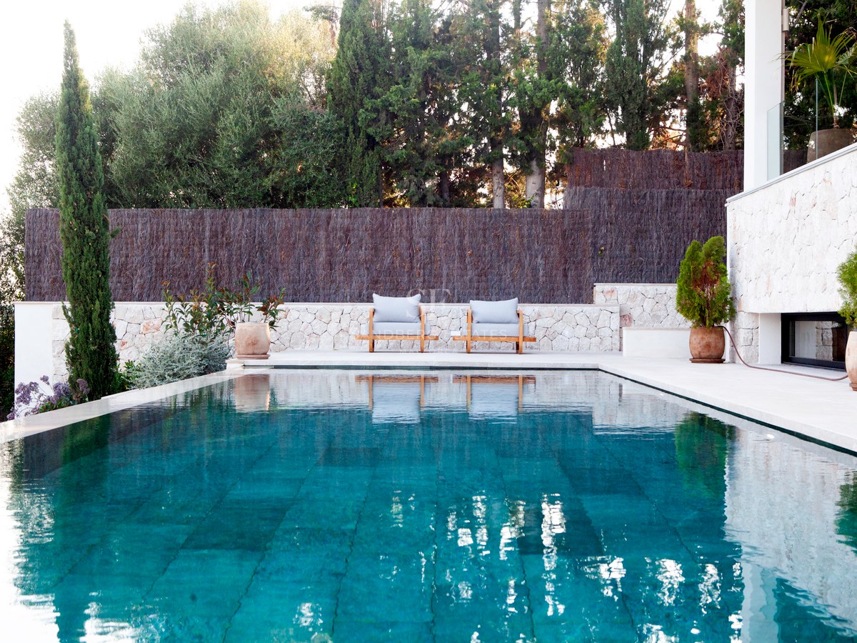 Türkisfarbener Infinity-Pool mit Natursteinumrandung, Holzliegen und üppigem mediterranem Garten.