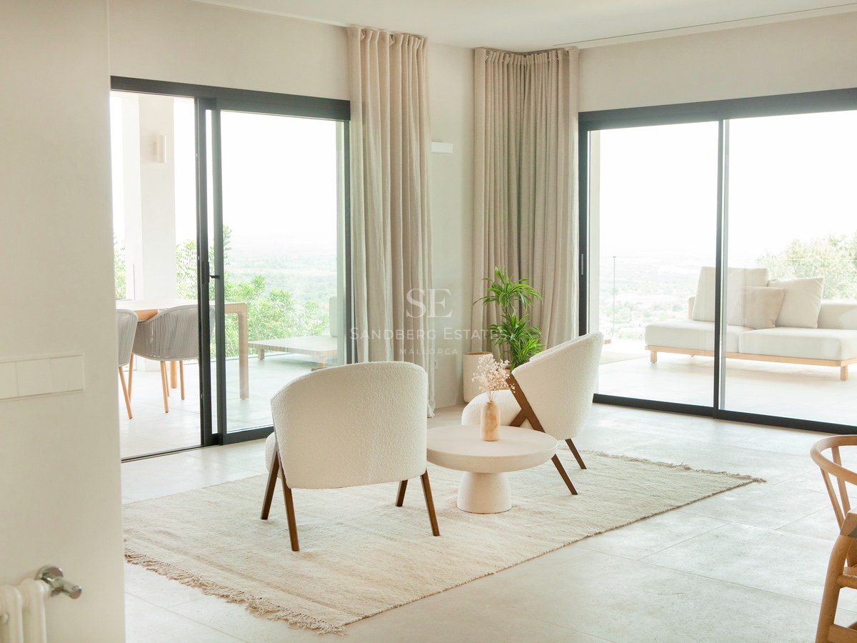 Modernes Wohnzimmer mit Bouclé-Sesseln, Steinboden und großen Glasschiebetüren, die auf eine sonnige Terrasse führen.