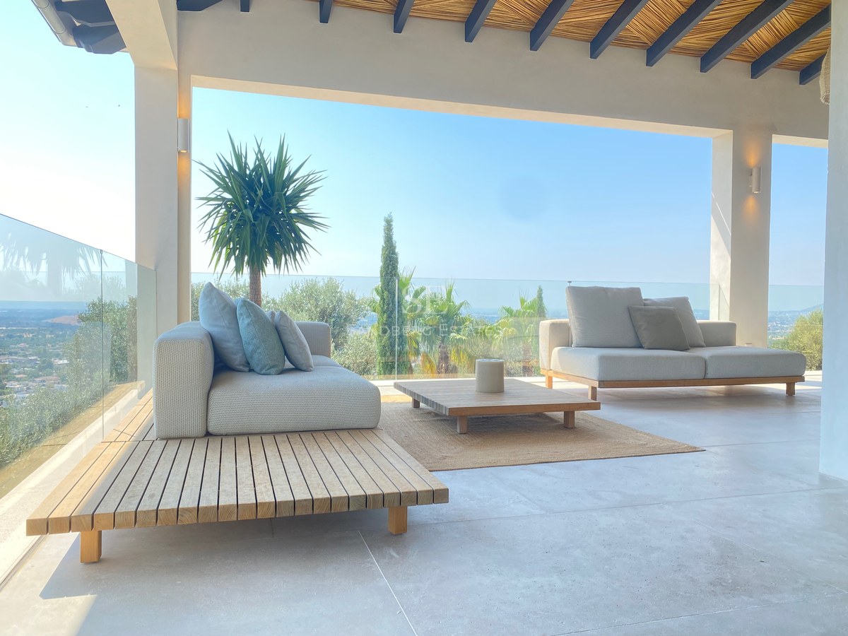 Luxuriöse Terrasse mit modernen Sofas, Holztisch, Glasgeländer und weitem Blick auf die Landschaft.